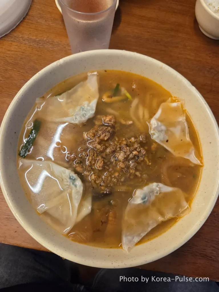 A steaming bowl of Kalguksu (knife-cut noodles) with minced meat topping and four dumplings, alongside a plate of signature Mandu at Myeongdong Kyoza, recognized as one of the Best Myeongdong Restaurants.