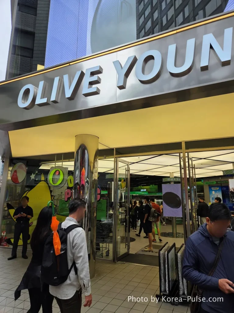 Close-up of the Olive Young Myeongdong Town entrance sign with a steady stream of international tourists entering the store