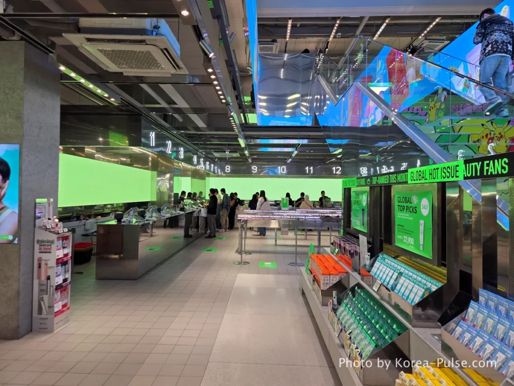 Olive Young Myeongdong Town first floor showing giant digital display screens and product shelves stretching the length of the store