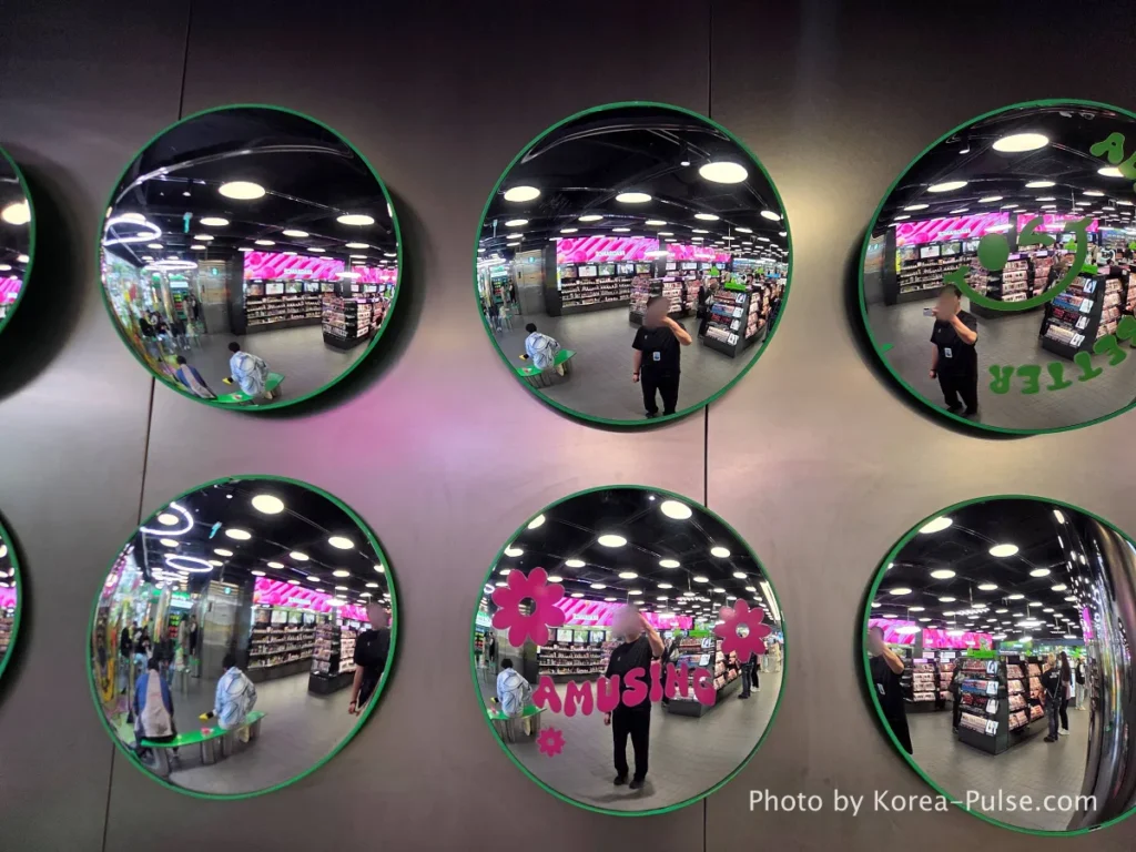 Row of large circular convex design mirrors mounted on the wall of Olive Young Myeongdong Town second floor reflecting the colorful makeup section interior