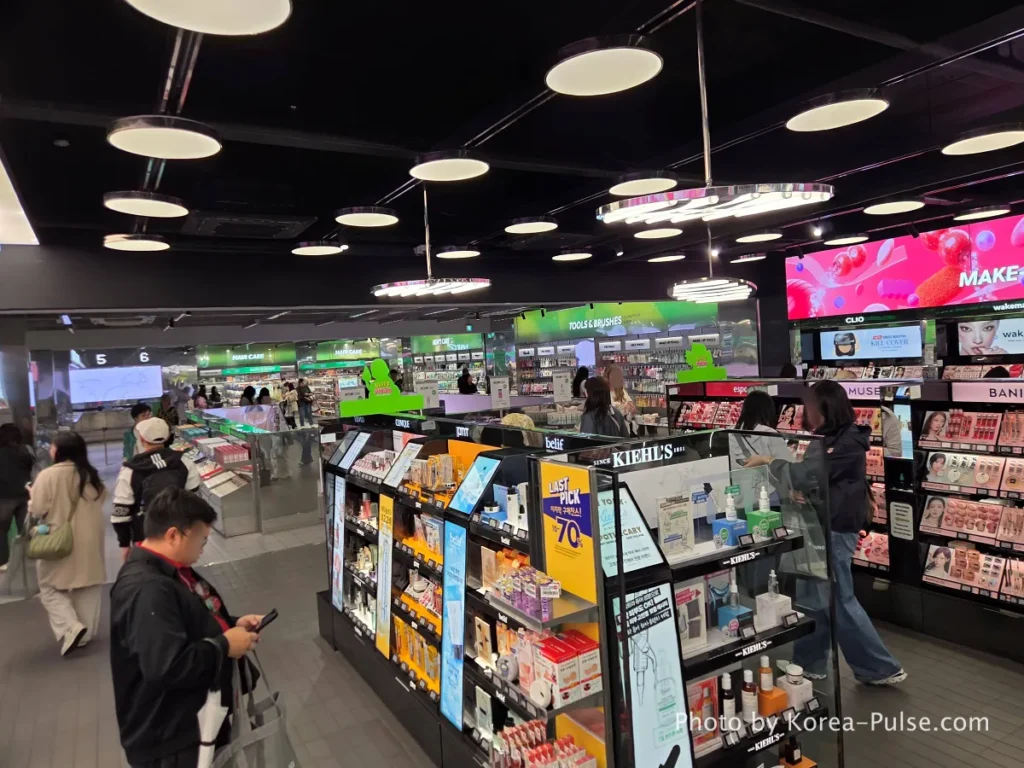 Wide panoramic view of the second floor of Olive Young Myeongdong Town dedicated to makeup and hair care products with shoppers browsing spacious dark-toned aisles