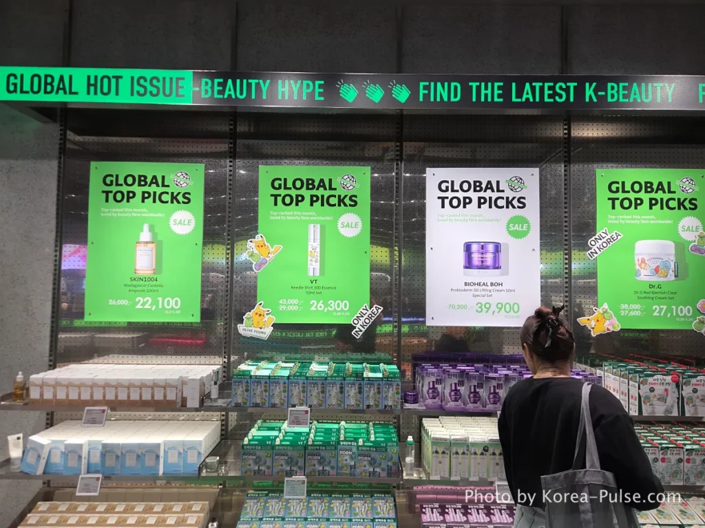 Olive Young Myeongdong Town Global Top Picks display section on the second floor curating the most popular K-beauty products among international shoppers with prominent signage. Large VT Reedle Shot advertisement display on the second floor of Olive Young Myeongdong Town showing the viral Korean skincare product prominently featured