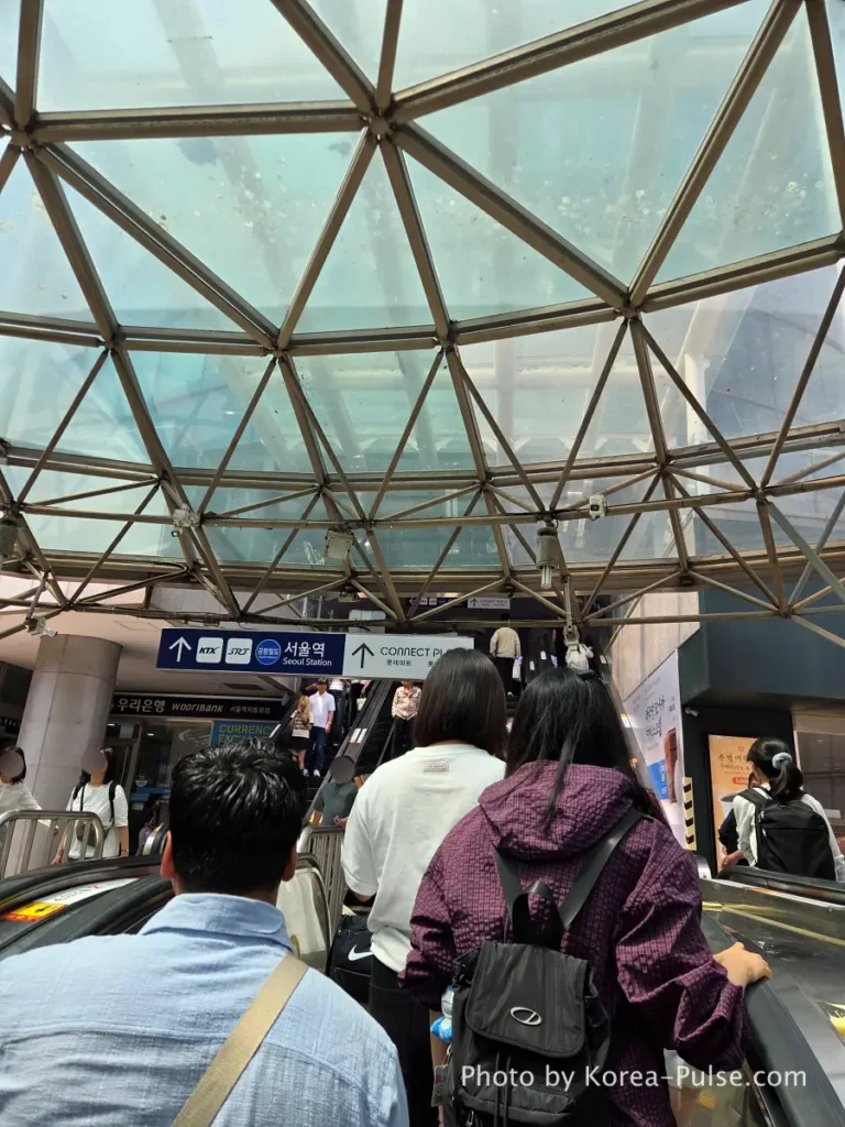Escalator rising toward the glass dome ceiling at Seoul Station with natural light streaming in from above