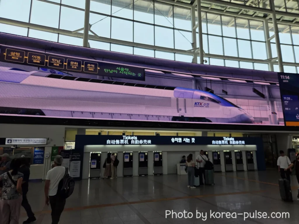 Seoul Station main hall showing the automated KTX ticket machines under the large Tickets sign, with a KTX train displayed on the giant LED screen above