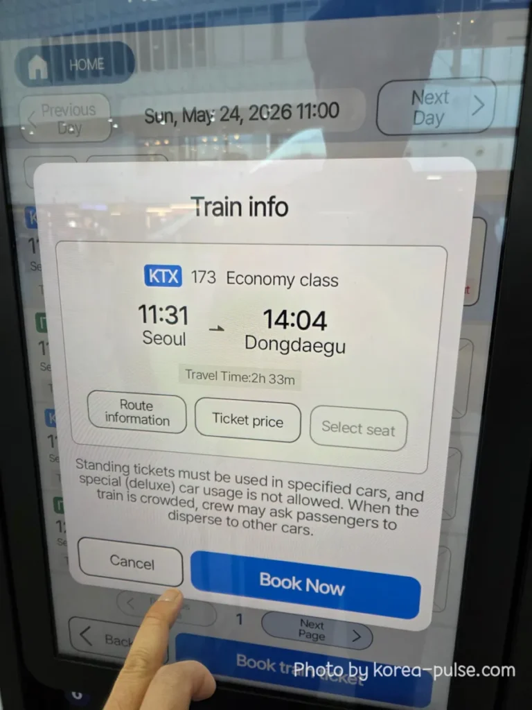Train info pop-up on the KTX ticket machine showing KTX 173 Economy Class departing Seoul at 11:31 and arriving Dongdaegu at 14:04 with a Book Now button at the bottom