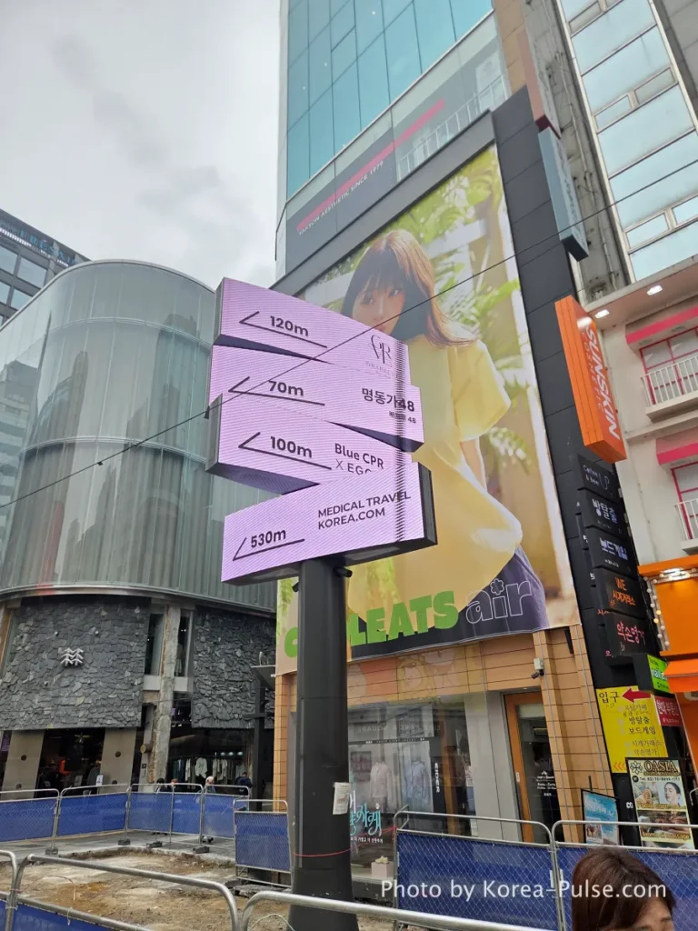 Myeongdong Street in May: Where Seoul's Best Food Hides in Plain Sight 8 Large new digital wayfinding signage pillar being installed in central Myeongdong street showing directions to nearby landmarks in metres