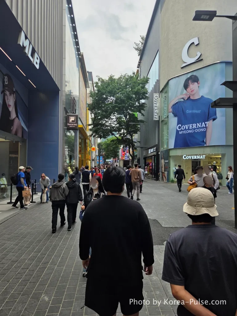 Myeongdong Street in May: Where Seoul's Best Food Hides in Plain Sight 9 Myeongdong shopping street with MLB and Covernat brand stores, pedestrians walking through tree-lined avenue in May