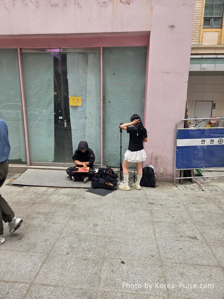 Myeongdong Street in May: Where Seoul's Best Food Hides in Plain Sight 6 Female content creator live streaming outdoors in Myeongdong street while male crew member manages broadcasting equipment on the pavement