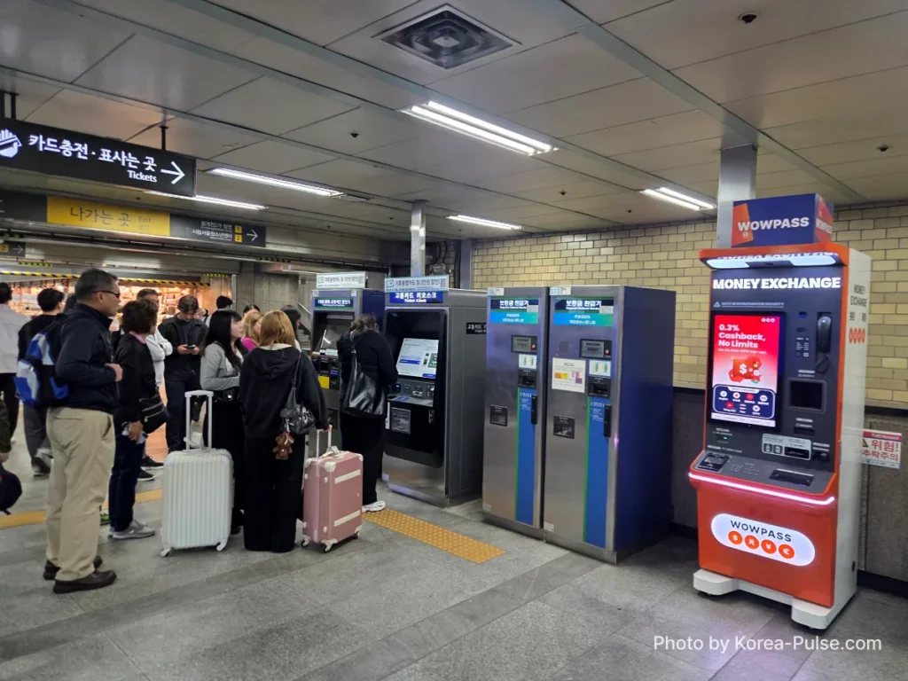 Multiple foreign visitors queuing at Seoul Metro ticket machines in Euljiro underground arcade to buy single journey subway tickets