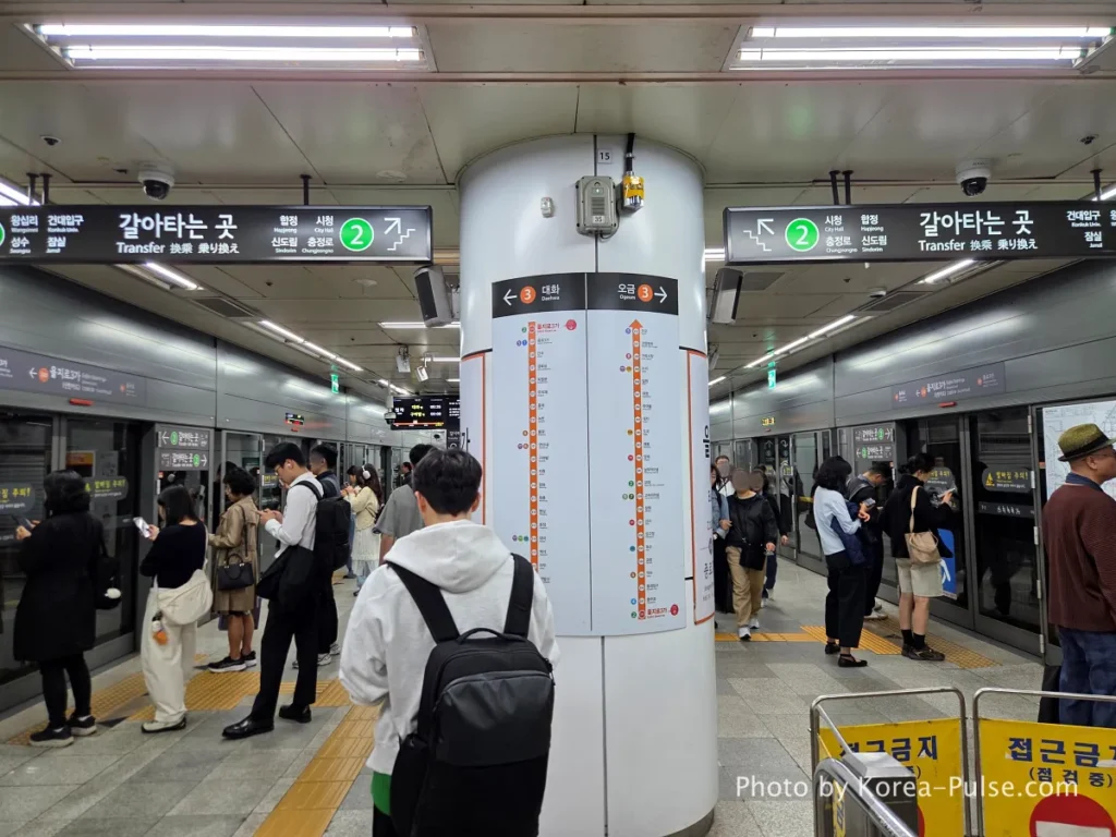 Seoul Metro platform with white central pillar showing route maps, passengers waiting on both sides in front of screen doors. Seoul Subway Guide: Rush Hour on Line 3