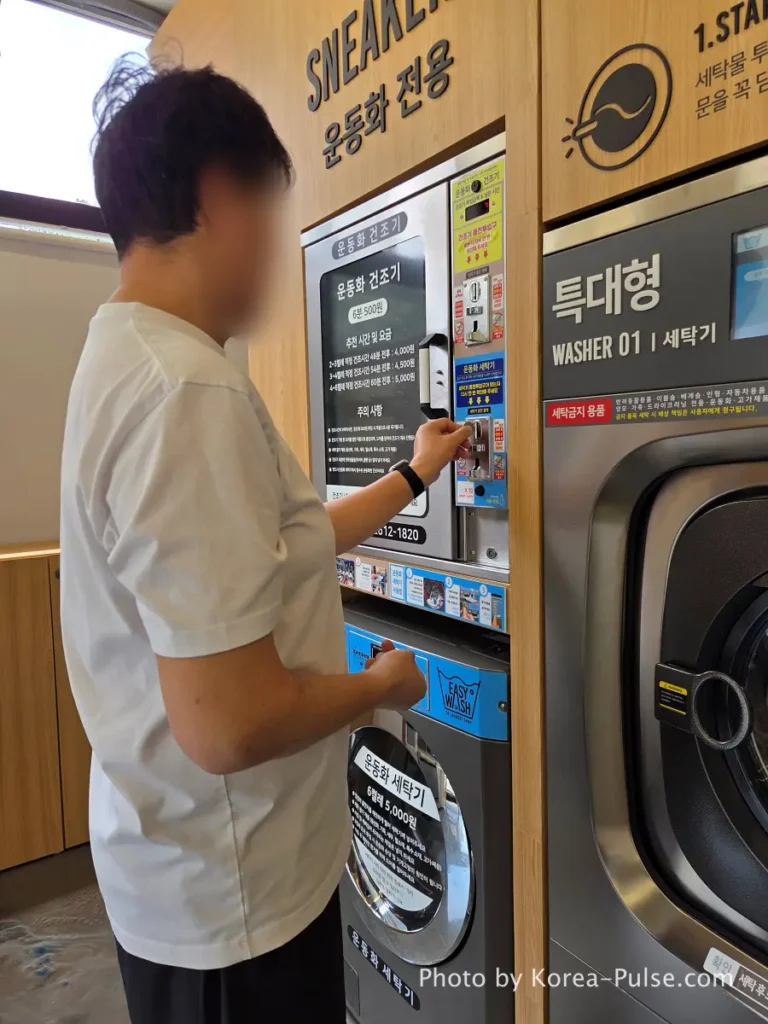 Coin Laundry in Korea: The Local's Complete Guide to 빨래방 11 Man inserting 500 won coins into blue coin control panel on sneaker washing machine at Easy Wash Korean coin laundry Seoul