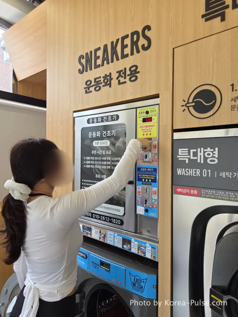 Coin Laundry in Korea: The Local's Complete Guide to 빨래방 14 Woman inserting coins into sneaker dryer upper unit at Easy Wash Korean coin laundry with large commercial dryers visible beside sneaker station