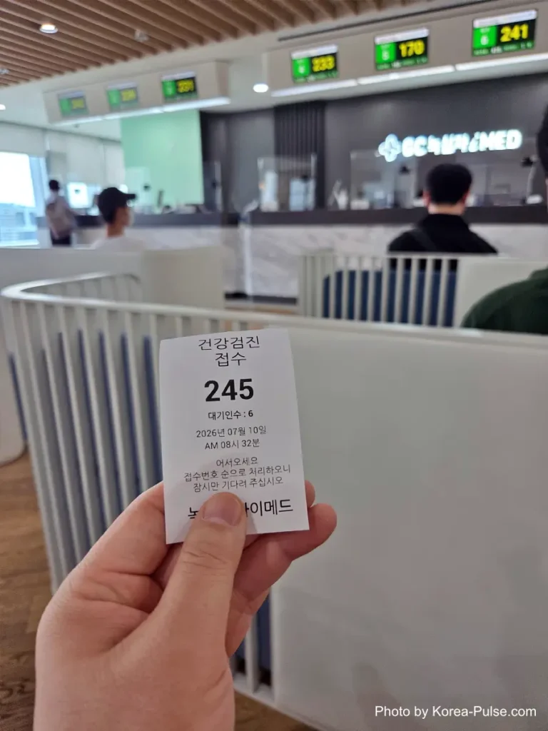 Inside Korea's 2-Hour Health Checkup Machine: Wristbands, Yellow Lines, and a Bowl of Porridge 2 Hand holding a paper queue ticket numbered 245 at a health checkup reception kiosk