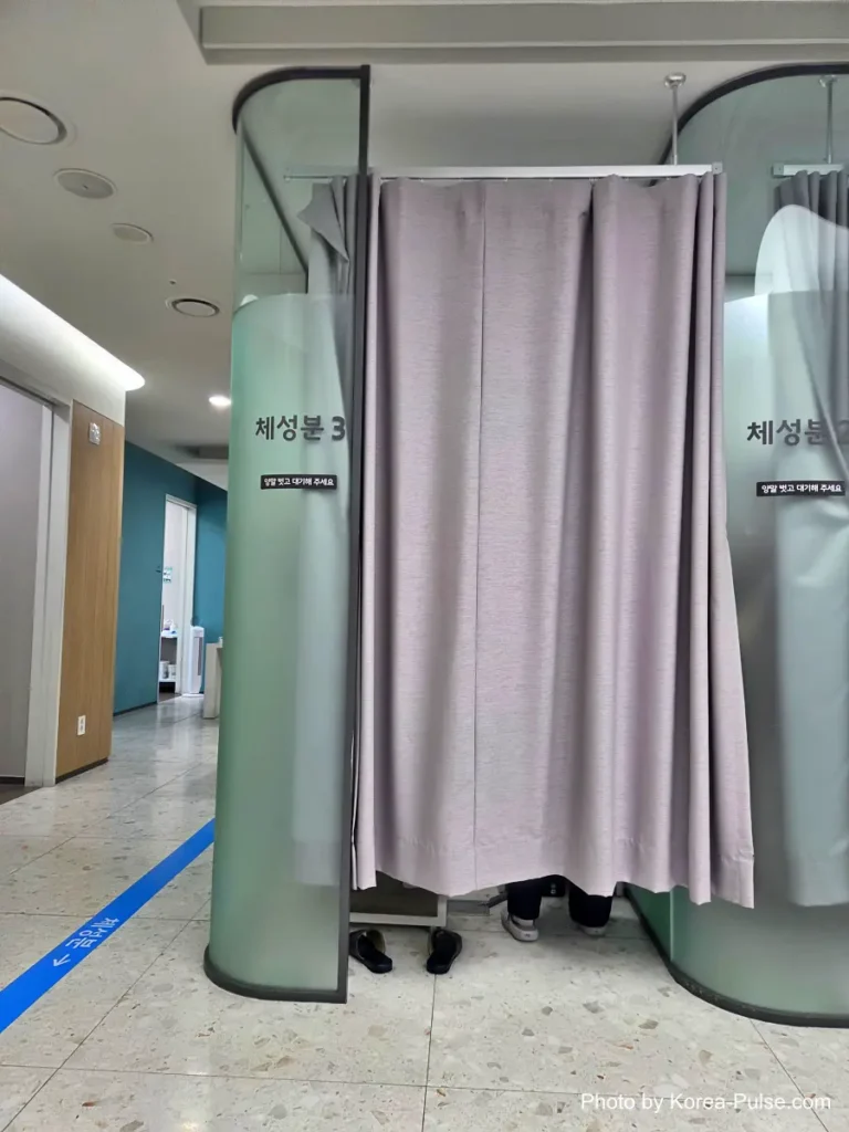 Inside Korea's 2-Hour Health Checkup Machine: Wristbands, Yellow Lines, and a Bowl of Porridge 8 Row of curtained booths with teal walls used for body composition measurements at a health checkup center