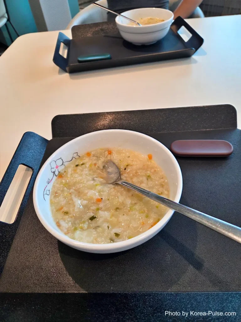 Inside Korea's 2-Hour Health Checkup Machine: Wristbands, Yellow Lines, and a Bowl of Porridge 16 A bowl of warm Korean rice porridge (juk) with a spoon, served on a tray table